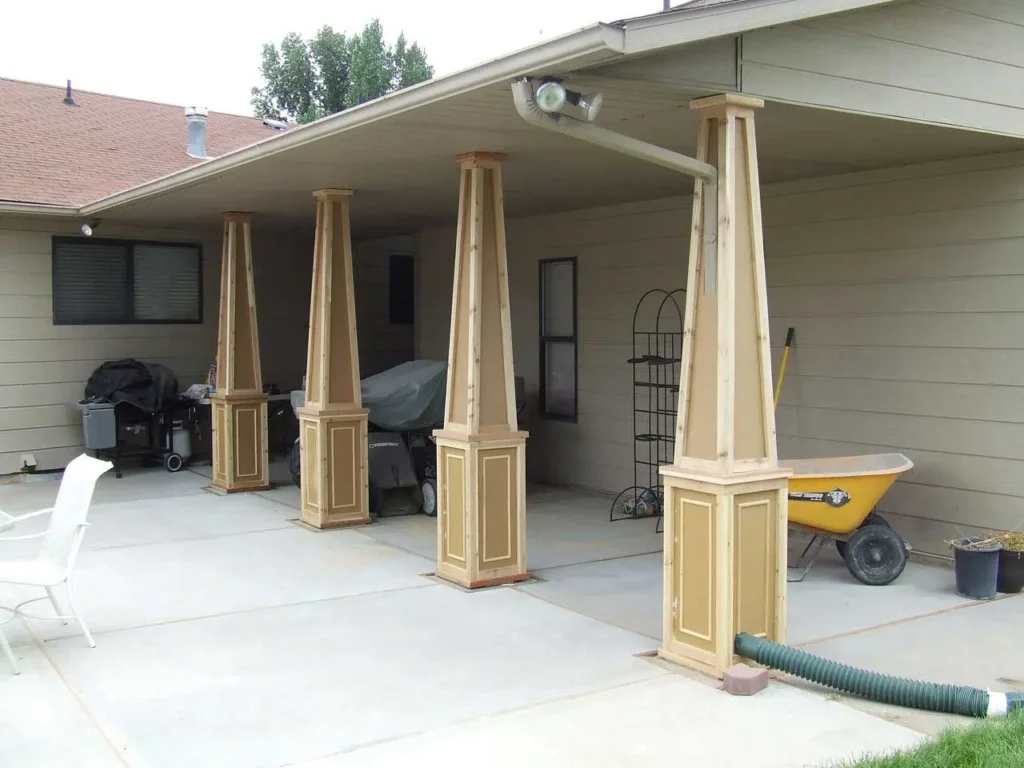 image shows a covered outdoor area, possibly a carport or patio, supported by four decorative wooden pillars